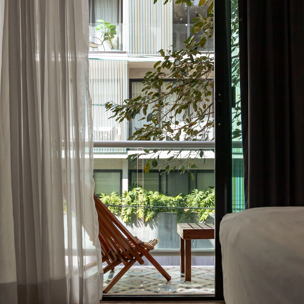 Window with white curtain, armchair, and green plants in a modern interior