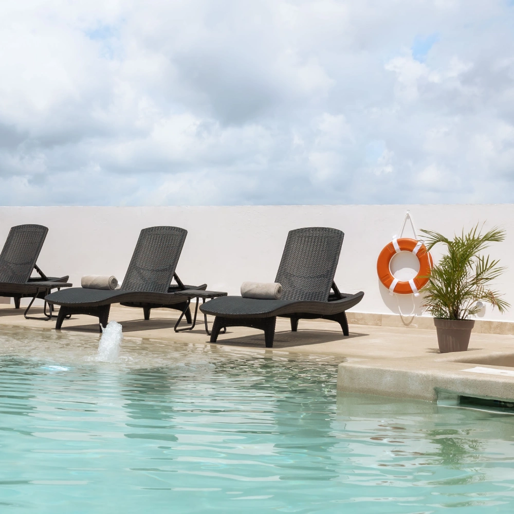 Pool with loungers and orange lifebuoy float, in front of a white wall.