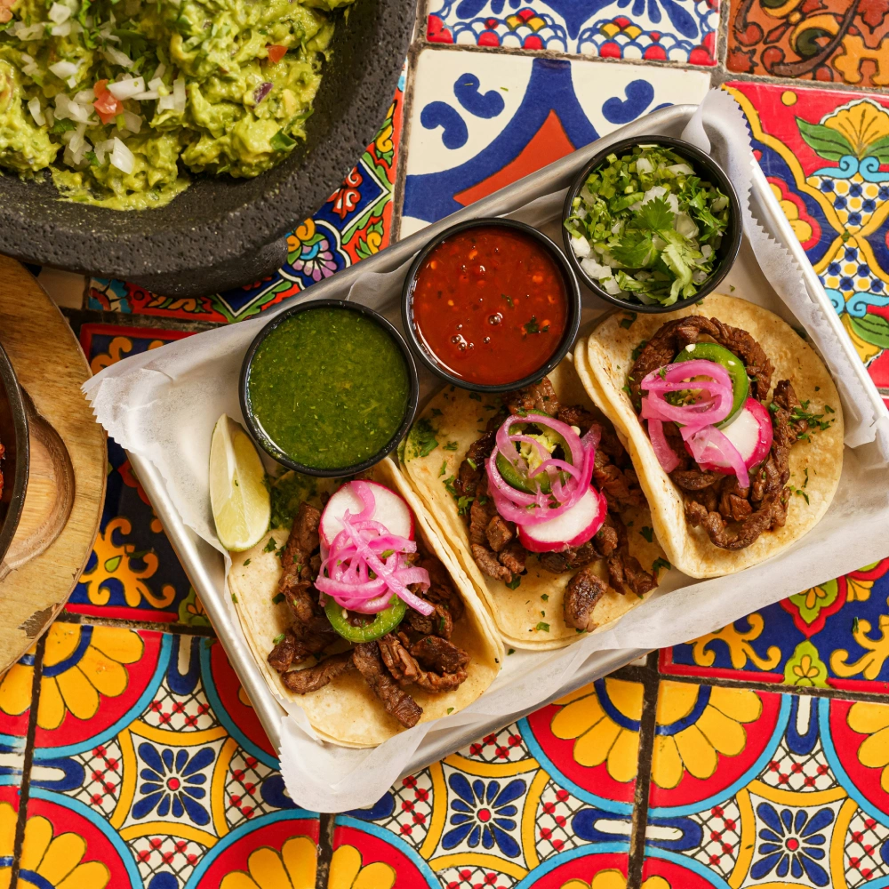 Tacos with meat, pickled radishes, two sauces and guacamole on colorful background